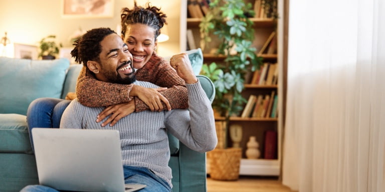 A young couple sitting together on the couch, reviewing their estate plan on a laptop resting on the man’s lap.
