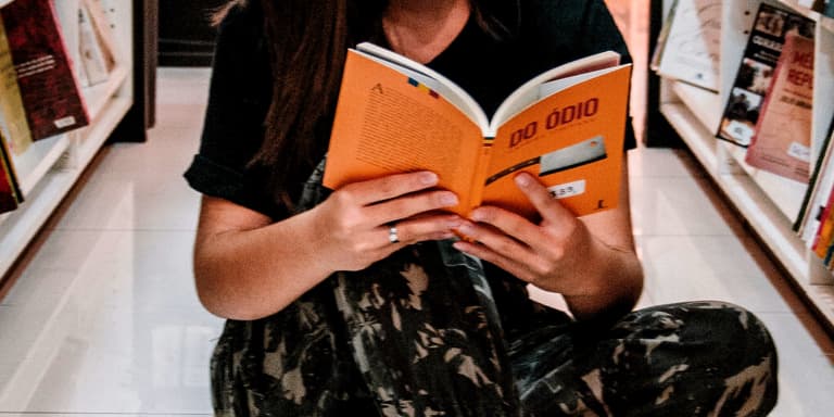 A lady sitting on the floor in an isle of a library reading a book