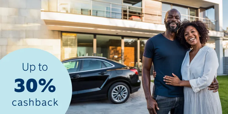 A smiling couple standing closely together in front of a modern house with a partial view of a vehicle, confident that their assets are protected with comprehensive car and home insurance.