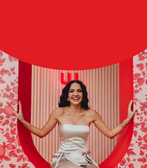 Miss South Africa 2023 Natasha Joubert in the She Owns Her Success studio, smiling and sitting inside a decorative circular cutout next to a red block of text defining 