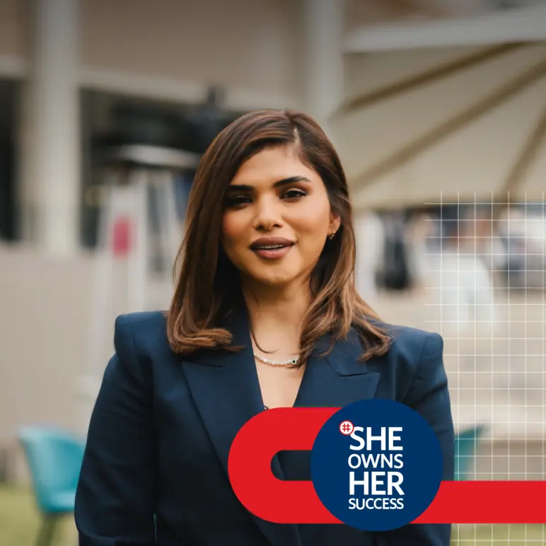 Portrait of a woman in a navy blazer and pearl necklace, attending the #SheOwnsHerSuccess Workshop in the background and featuring the campaign's logo. 