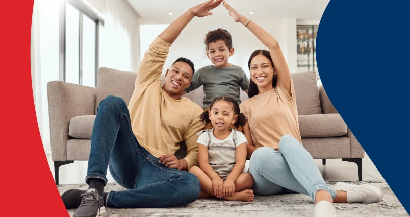 A smiling family of four sitting together in their living room, with the parents using their arms to form a protective roof shape over their children, representing the financial security and peace of mind that estate planning provides.