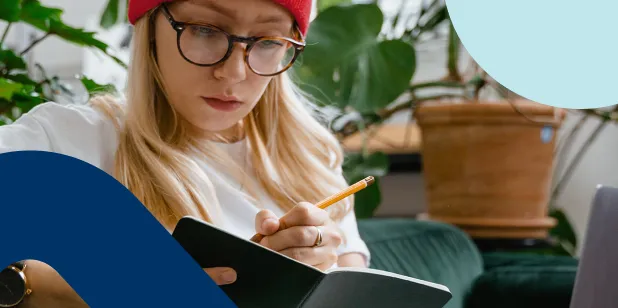A lady wearing reading glasses writing down her financial goals and savings plan in a notebook.