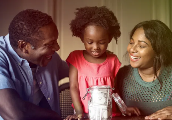 A smiling family of three gathered around a glass jar, filled with savings, symbolising financial planning and saving habits.