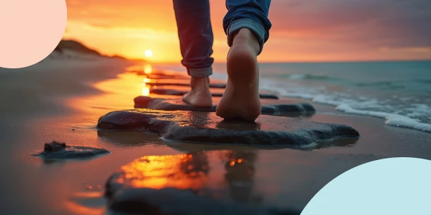 Close-up of a person walking barefoot on smooth stepping stones along a beach at sunset, showing a clear path forward to make smarter decisions with financial advice.