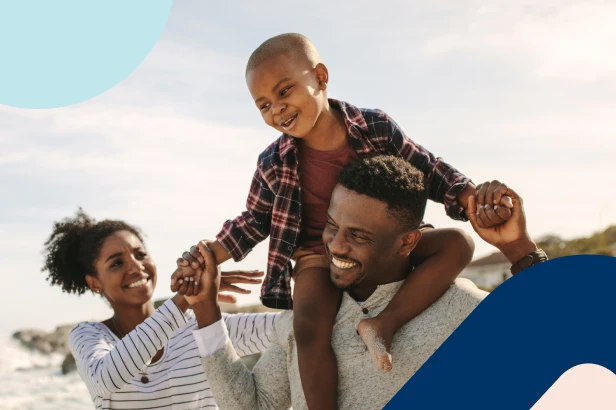 A family enjoys a day at the beach, with the little boy sitting happily on his dad’s shoulders.