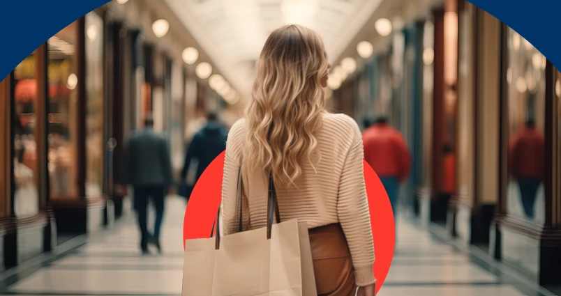 A woman with blonde wavy hair walking through a luxury shopping mall arcade holding shopping bags, symbolising lifestyle creep and spending more as income increases.