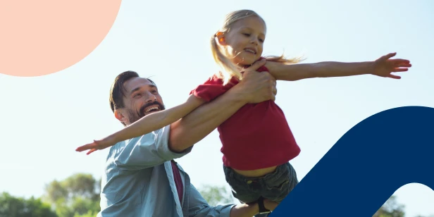 Father lifting and playing with his young daughter outdoors on a sunny day.