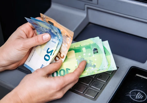 Close-up of cash being handled at an ATM with a blue and red overlay, representing the increase in early retirement savings withdrawals under the current two-pot retirement system regulations.