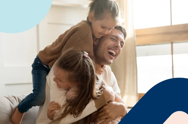 A happy father laughing with his two young daughters at home, confident that he has started instilling the importance of financial literacy in their daily activities.