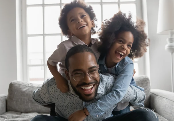 A smiling father spending quality time with his young son and daughter at home, symbolic of the important role father’s play in children’s financial journey from a young age.