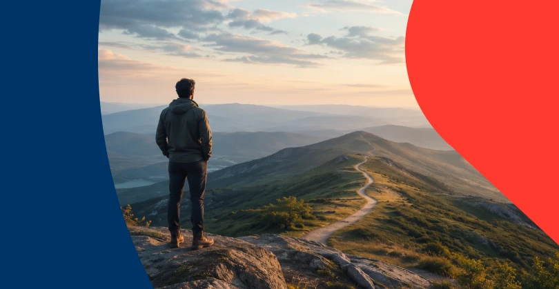 A man standing on a mountain peak looking down a long winding trail, symbolising the growth journey of long-term saving, which can yield results through financial advice.