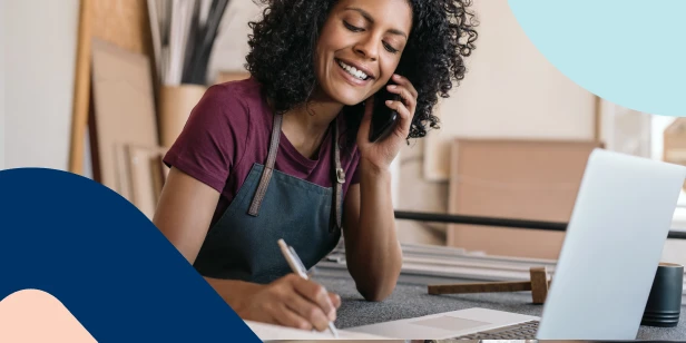 A smiling female content creator working on her laptop and phone, representing the confidence and freedom found through long-term financial security.