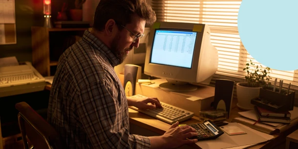 A side profile of a gen x man using a vintage computer and calculator for financial planning.