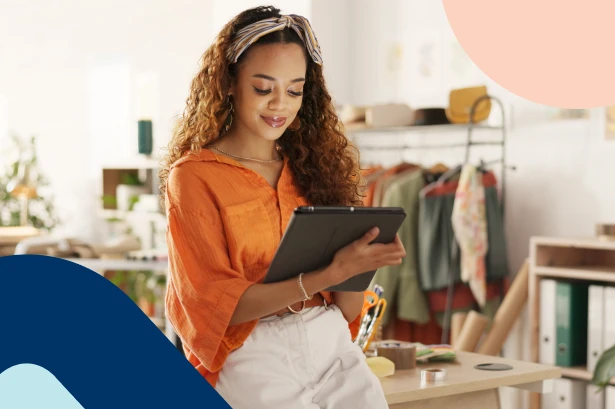 A young female freelancer with curly hair using a tablet in her creative studio, representing an independent professional planning her own retirement benefit package.