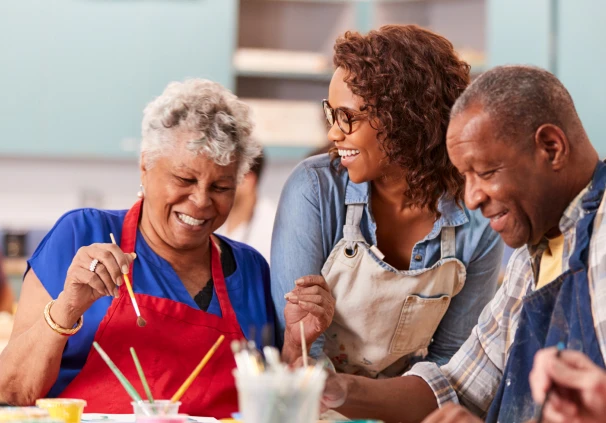 A retired couple attending an art class with a female instructor, enjoying a retirement hobby made possible through their retirement savings.
