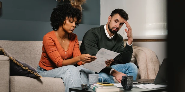 A young couple sits on a couch reviewing their retirement plans to help them avoid the retirement debt crisis that many South African retirees face.