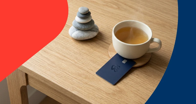 A serene tabletop scene featuring a stack of balanced Zen stones and a steaming cup of tea on a wooden surface, with a bank card resting nearby to symbolize the link between saving and self-care.