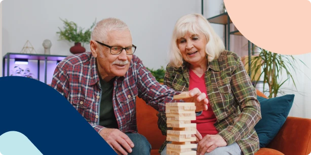 A senior couple playing a wooden block stacking game, representing the careful and consistent building of retirement savings to ensure long-term financial stability.