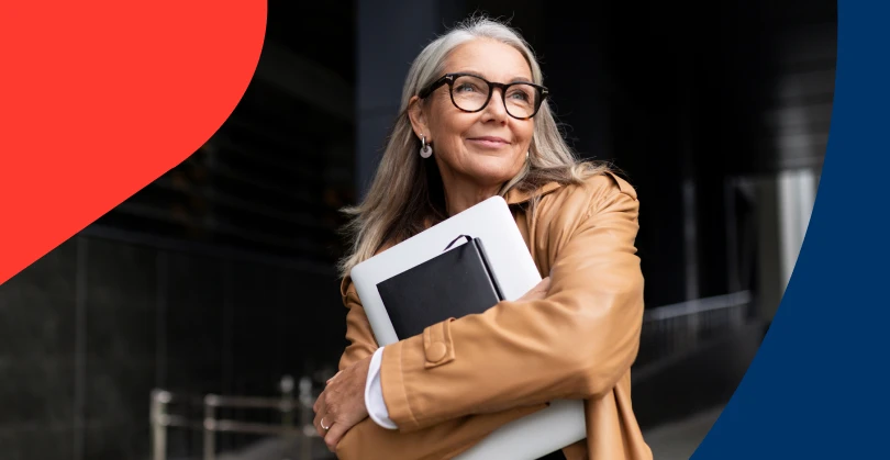A smiling, confident and successful senior businesswoman holding a laptop, conveying the wisdom of timeless money lessons.