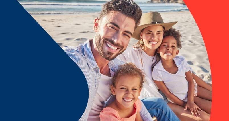 A happy family of four taking a smiling selfie together on a sunny beach.