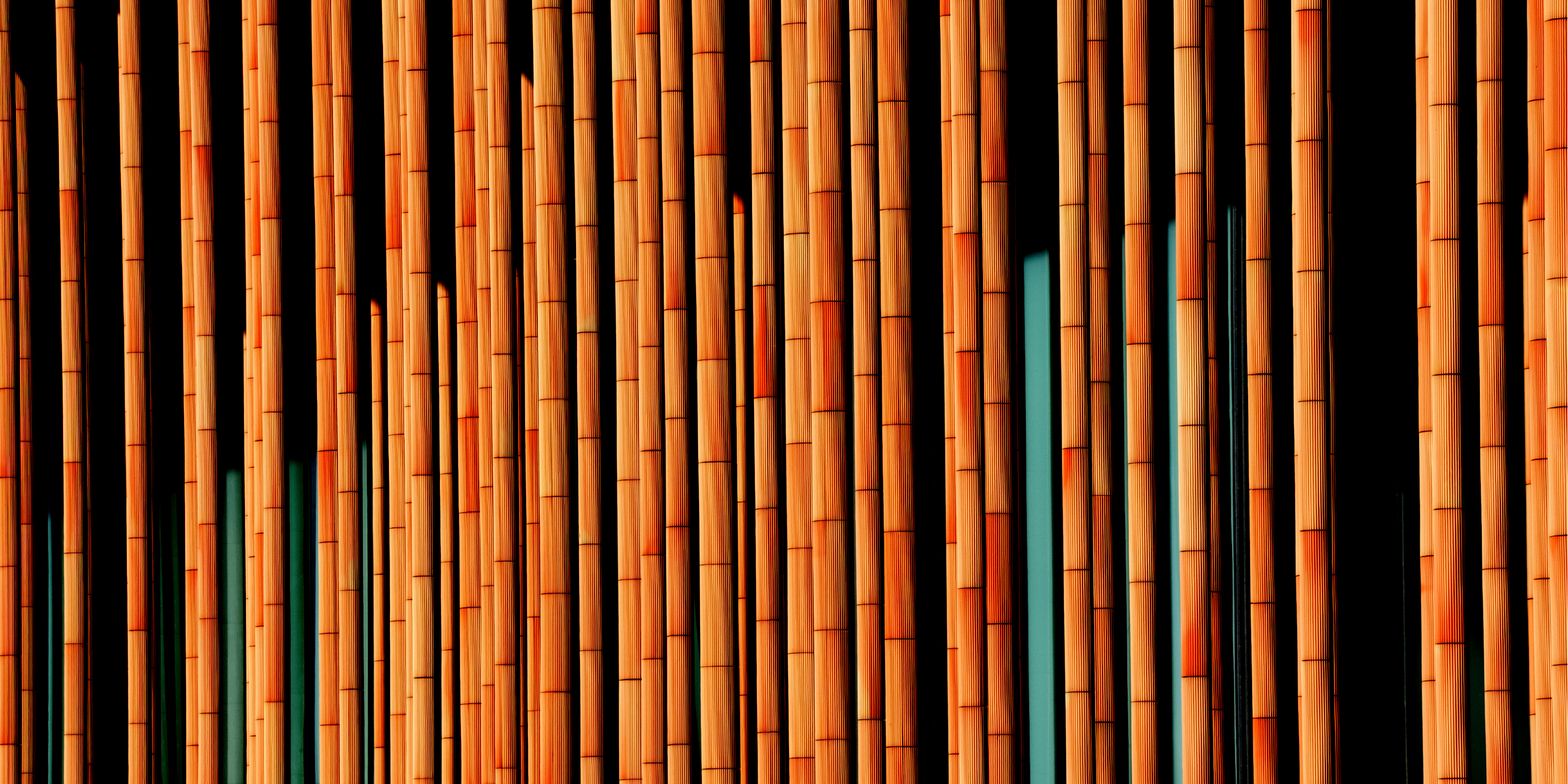 Boost your retirement savings: A close-up architectural shot showing a dense sequence of vertical, ribbed orange columns lit by warm sunlight against a dark background, creating a striped pattern of light and shadows.  