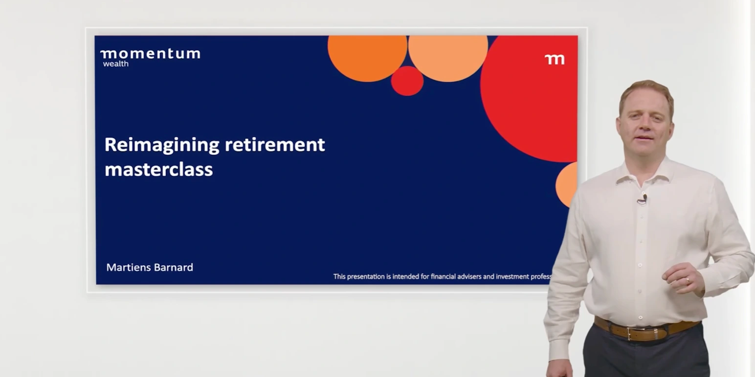 A presenter stands beside a slide titled “Reimagining retirement masterclass” branded with Momentum Wealth, featuring bold white text on a dark blue background with orange and red circular design elements. The presenter wears a light-coloured shirt and dark trousers, speaking in front of a clean white backdrop.