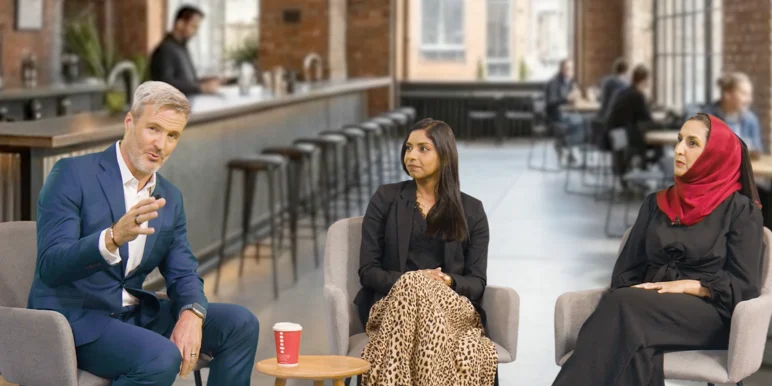 An older man in a blue suit gestures as he speaks to two women in a modern office lounge. One woman wears a leopard-print skirt while the other wears a black dress and red hijab. A red coffee cup is visible.