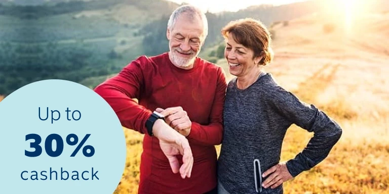 An elderly couple out on a hike on a sunny day as they look at the husband's smartwatch. 