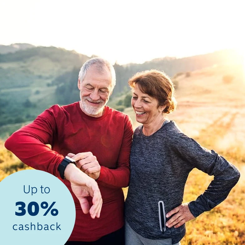 An elderly couple out on a hike on a sunny day as they look at the husband's smartwatch. 