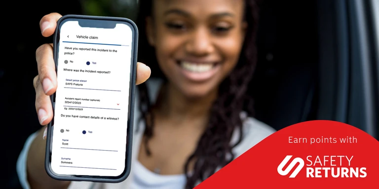A young woman is smiling and holding her cell phone as she sees that she has earned Safety Returns for submitting her car insurance claim through the Momentum App.