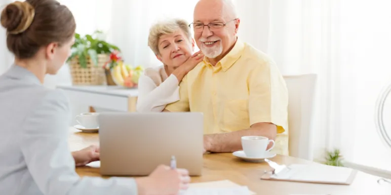 An elderly couple sitting with a short-term financial adviser, reviewing information together on a laptop.]
