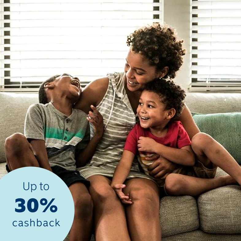 A young mother sitting on a couch and cuddling her two  young toddlers, happy and confident that all her belongings  are insured with a 30% cashback benefit.