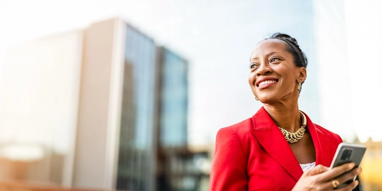 Confident woman in a red blazer holding a smartphone in the city representing market-linked living annuity investments from Momentum. 