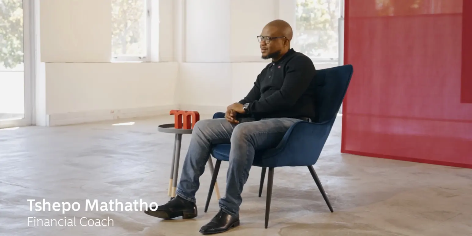 Tshepo Mathatho, a Financial Coach at Momentum Corporate, speaking about employee benefits while seated in a blue armchair.
