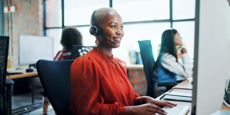 Call center staff, sitting at their work stations with their headphones on,  attending to client phone calls.