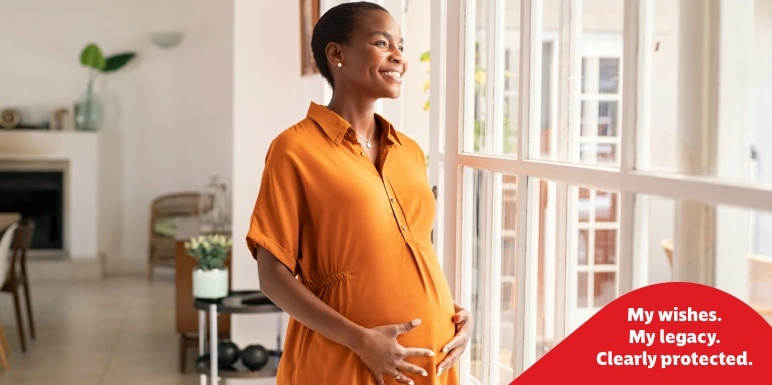 A pregnant woman in an orange dress cradling her baby bump near a window, confident that she has legacy planning and an estate protection plan in place to secure her legacy.