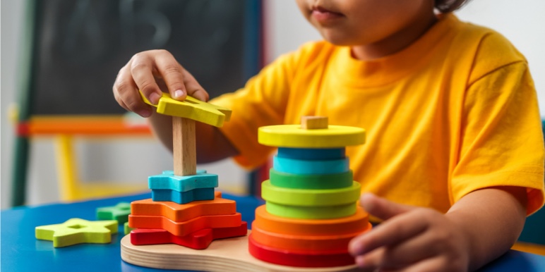 Child playing with colourful building blocks, symbolising saving for education and future goals.