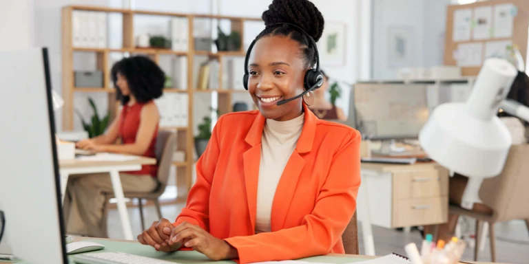 A smiling consultant with a headset sits at a desk in a modern office, providing customer support for two-pot savings withdrawals.