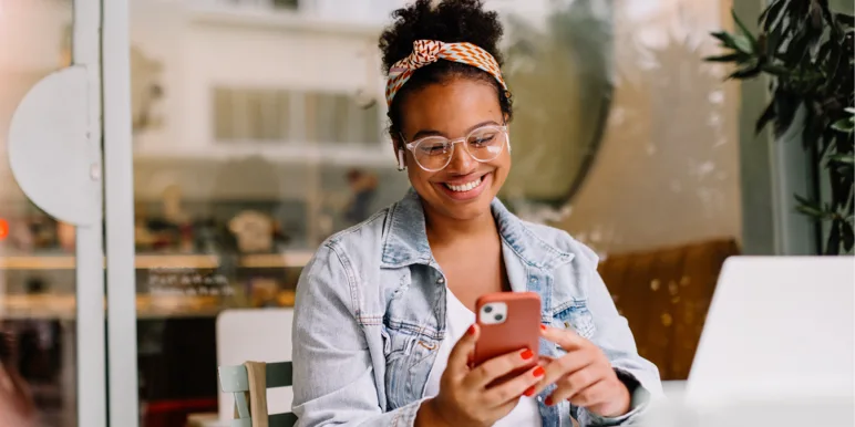 A smiling woman in a cafe uses her phone to manage two-pot withdrawals via WhatsApp.