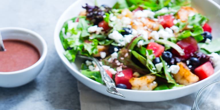 A bowl of green salad with a side bowl of dressing placed on a table. 