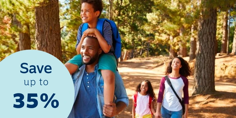 Young mom and dad are walking in the park. The dad is carrying his son on his shoulders.