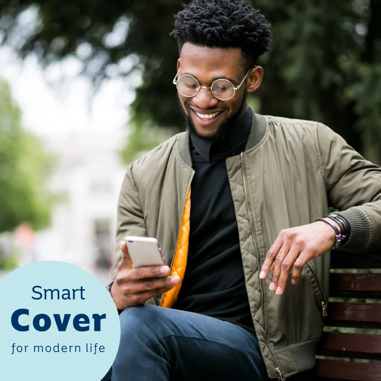 Young man sitting on a bench outdoors, smiling while looking at his cell phone, reading up on Momentum’s Evolve medical aid option.