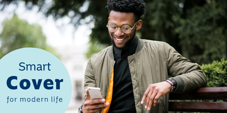 Young man sitting on a bench outdoors, smiling while looking at his cell phone, reading up on Momentum’s Evolve medical aid option.