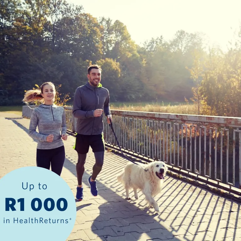 A young couple staying active to earn Momentum Health Returns. They’re jogging across a bridge while the man holds a white dog on a dog leash.