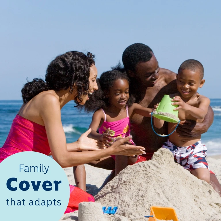 Mother and father happily playing on the beach with their two children in the sand building a sandcastle, near the ocean.