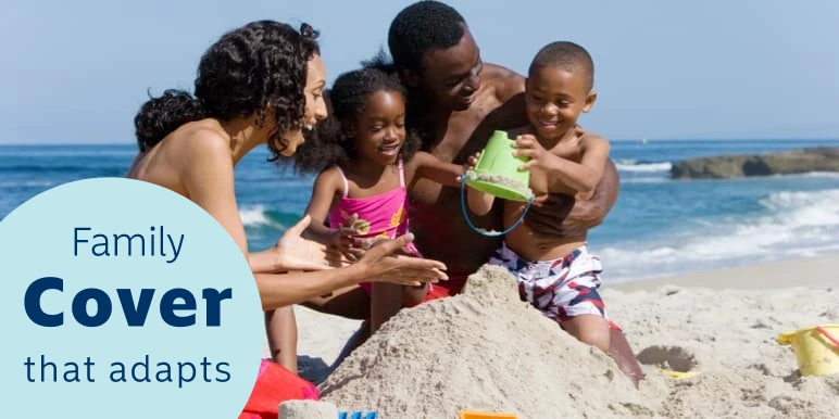Mother and father happily playing on the beach with their two children in the sand building a sandcastle, near the ocean.