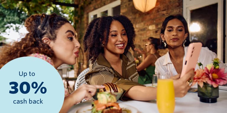 3 ladies looking at a smartphone over brunch, showcasing the peace of mind and financial freedom that comes with bundled car and home insurance.