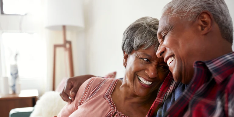A happy senior couple laughing together at home, showcasing the peace of mind that comes with growing your retirement savings thanks to tax incentives.