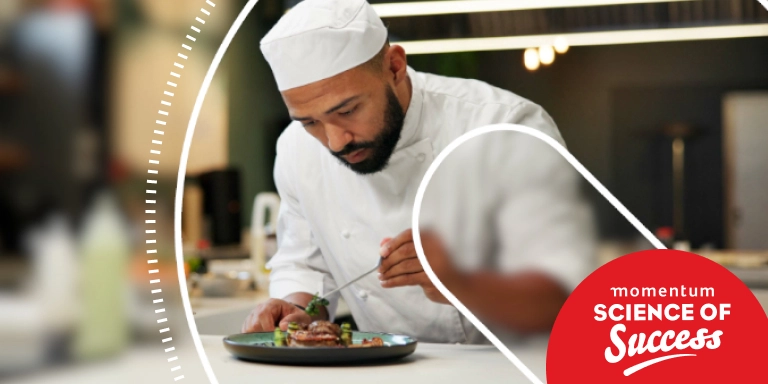 A chef carefully adds the final garnish to a plated dish, moving with precision and unwavering focus.